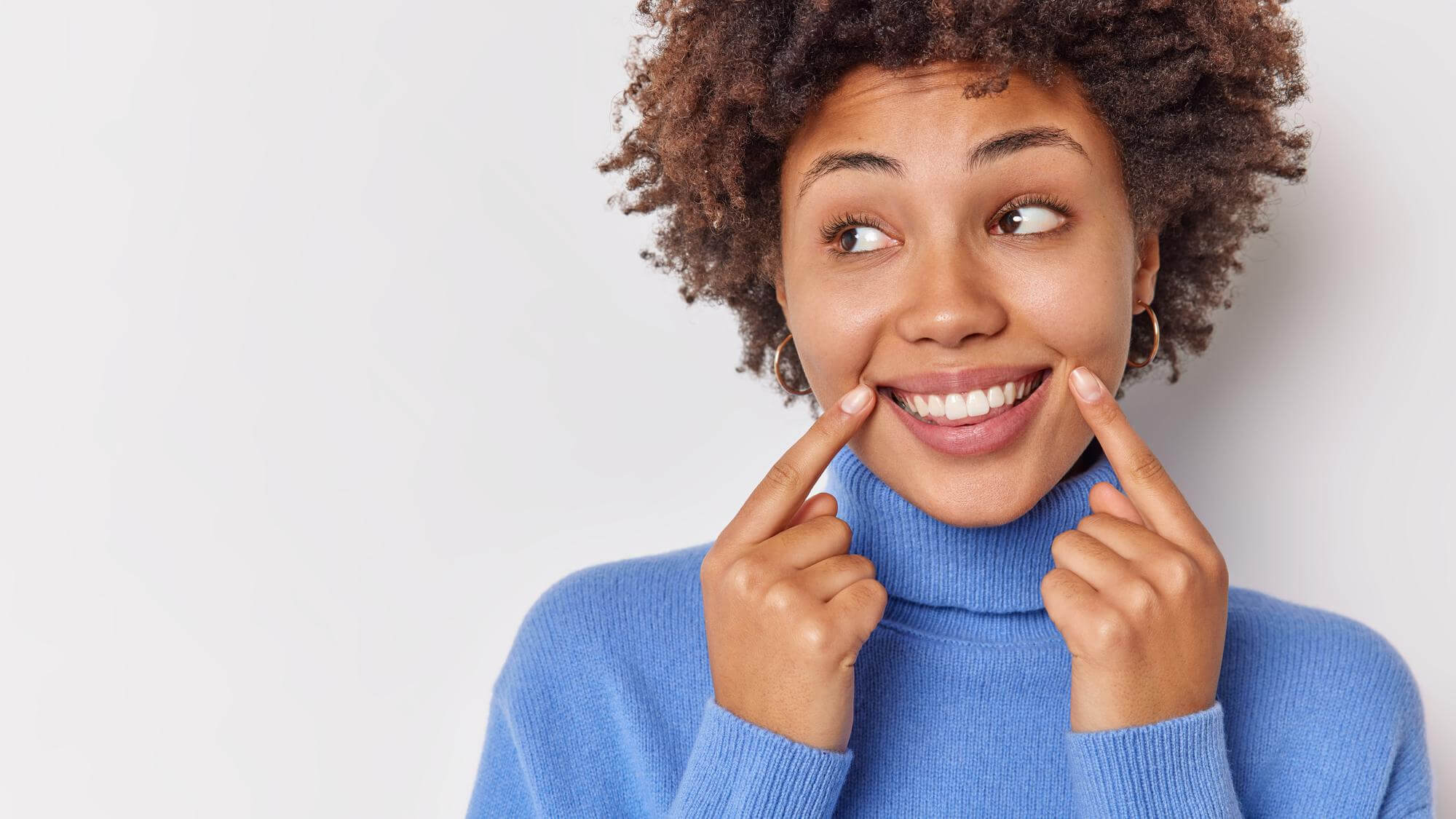 woman smiles broadly points her perfect even teeth with good oral health
