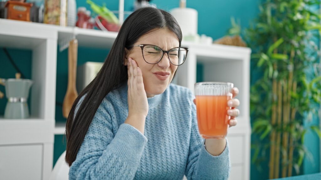 women drinking juice while holding her jaw in discomfort